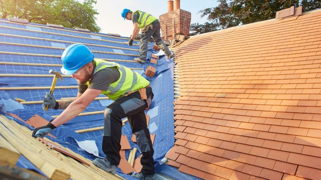 Workers installing roof tiles on a building.