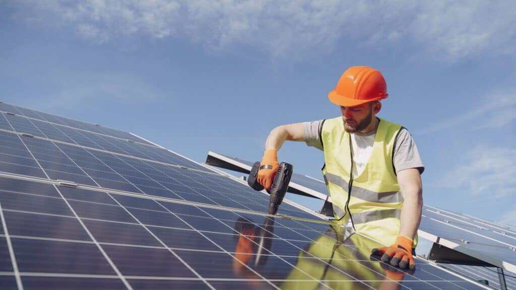 Worker installing solar panels with a drill.