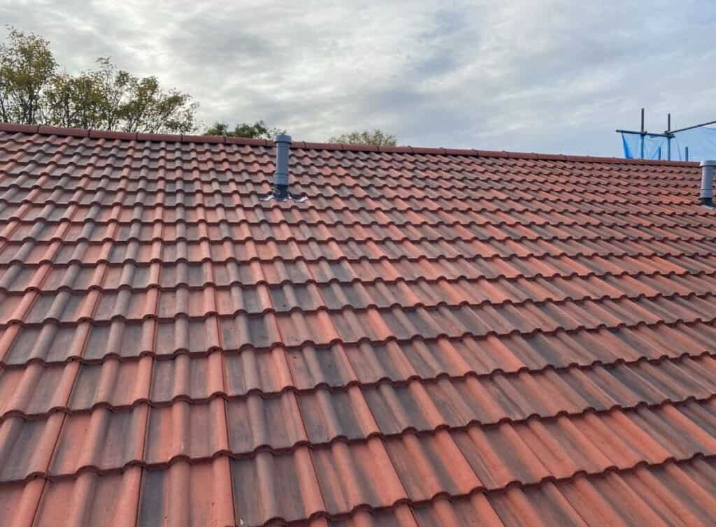 Red tile roof with chimneys under cloudy sky.