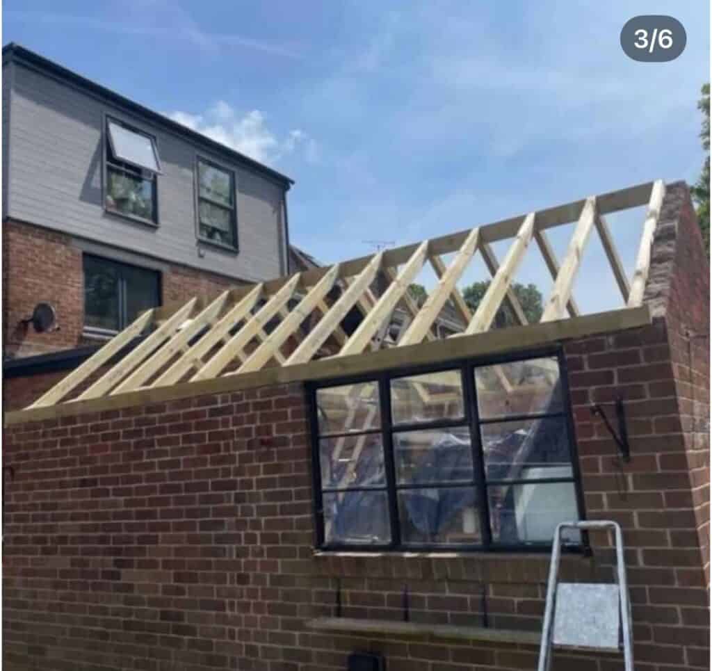 Partially constructed wooden roof frame on brick building.