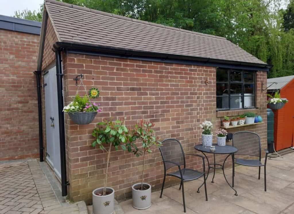 Garden shed with patio and potted plants.