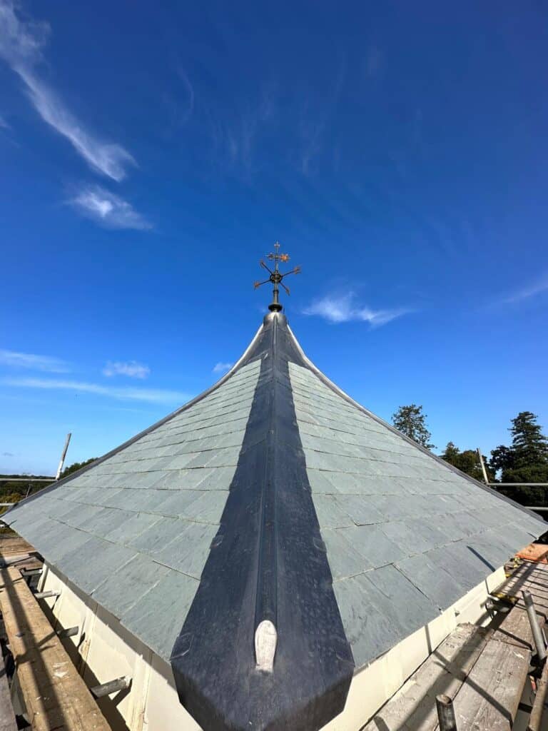 Slate roof with weather vane against blue sky.