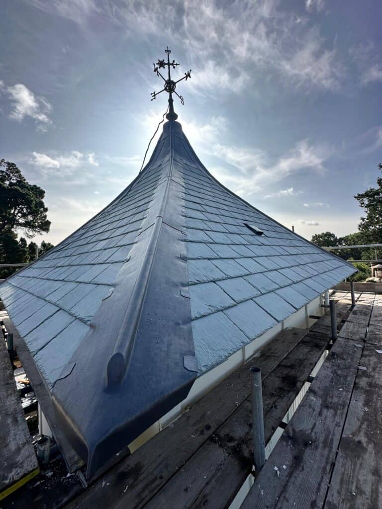 Church steeple with weathervane against cloudy sky.