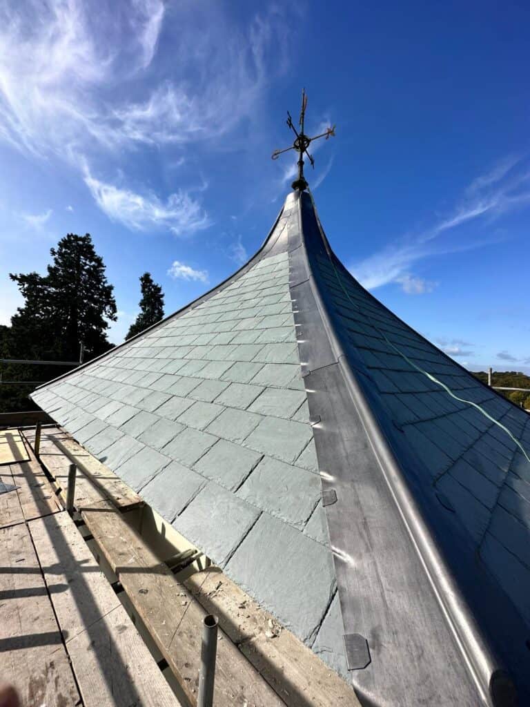 Weather vane atop slate roof against blue sky.