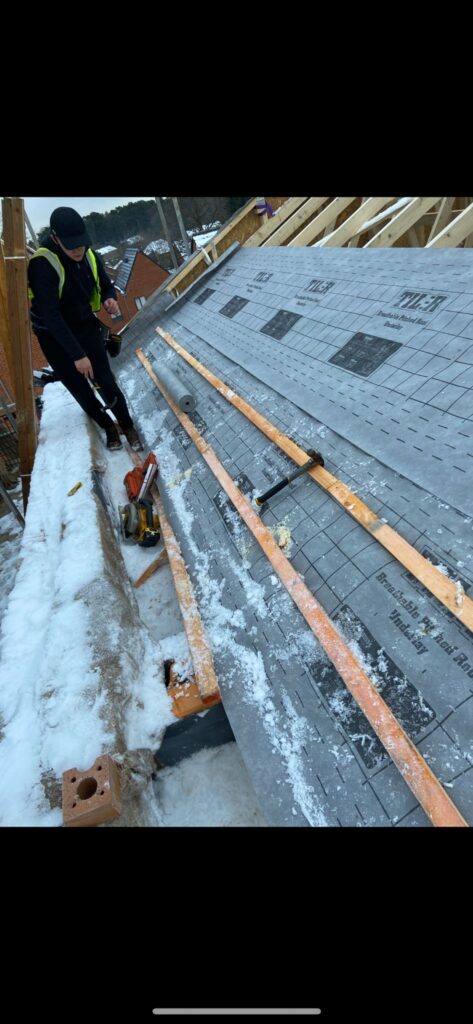 Worker installing roof underlayment in snow.