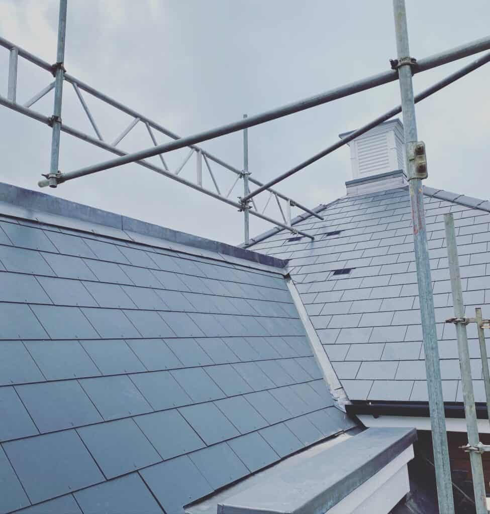 Scaffolding on slate tiled roof under cloudy sky.