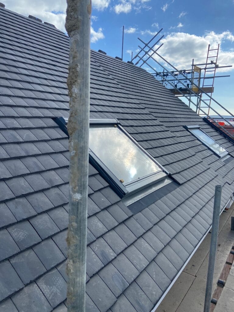 Scaffolded roof with skylight and tiles, blue sky.