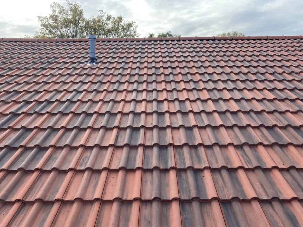 Red roof tiles with chimney and cloudy sky.