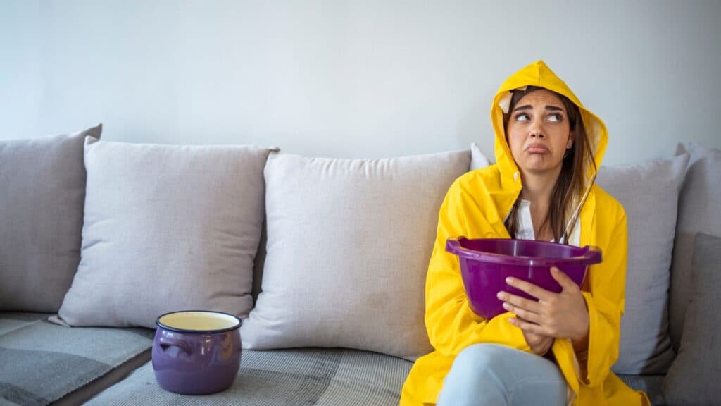 Woman in raincoat holding bucket indoors.