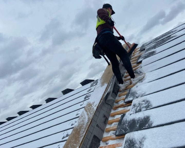 Worker clearing snow from rooftop.