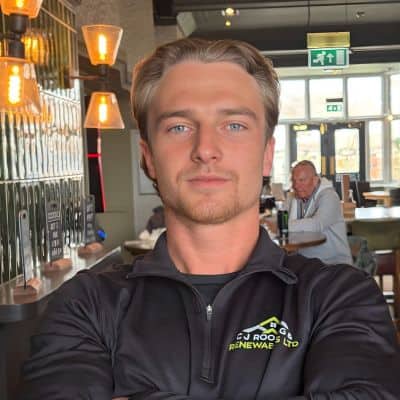 Portrait of Jack Shaw, co-owner of C J Roofing & Renewables, wearing a branded zip-top in a pub interior.