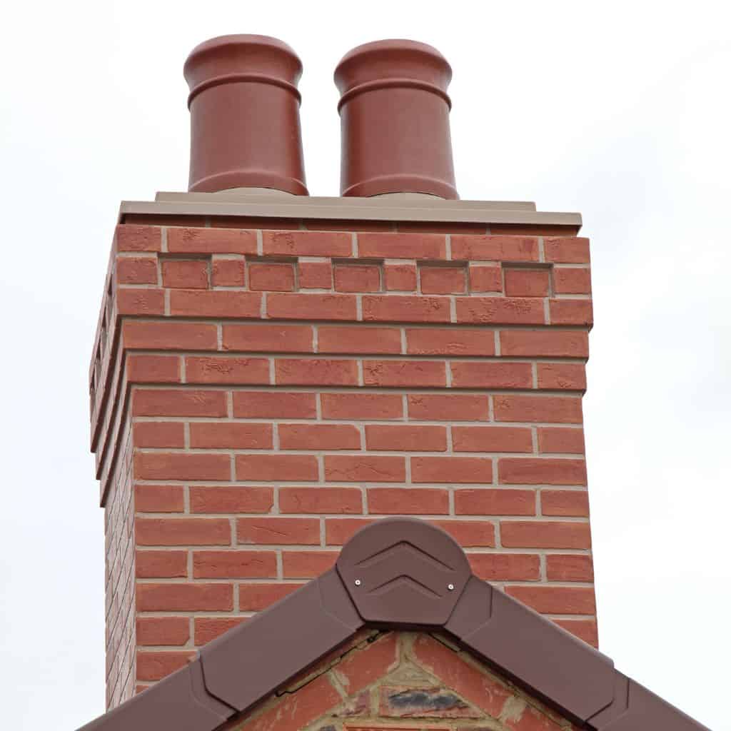 Newly rebuilt red brick chimney stack with two terracotta pots and stone capping, set against a plain white sky.
