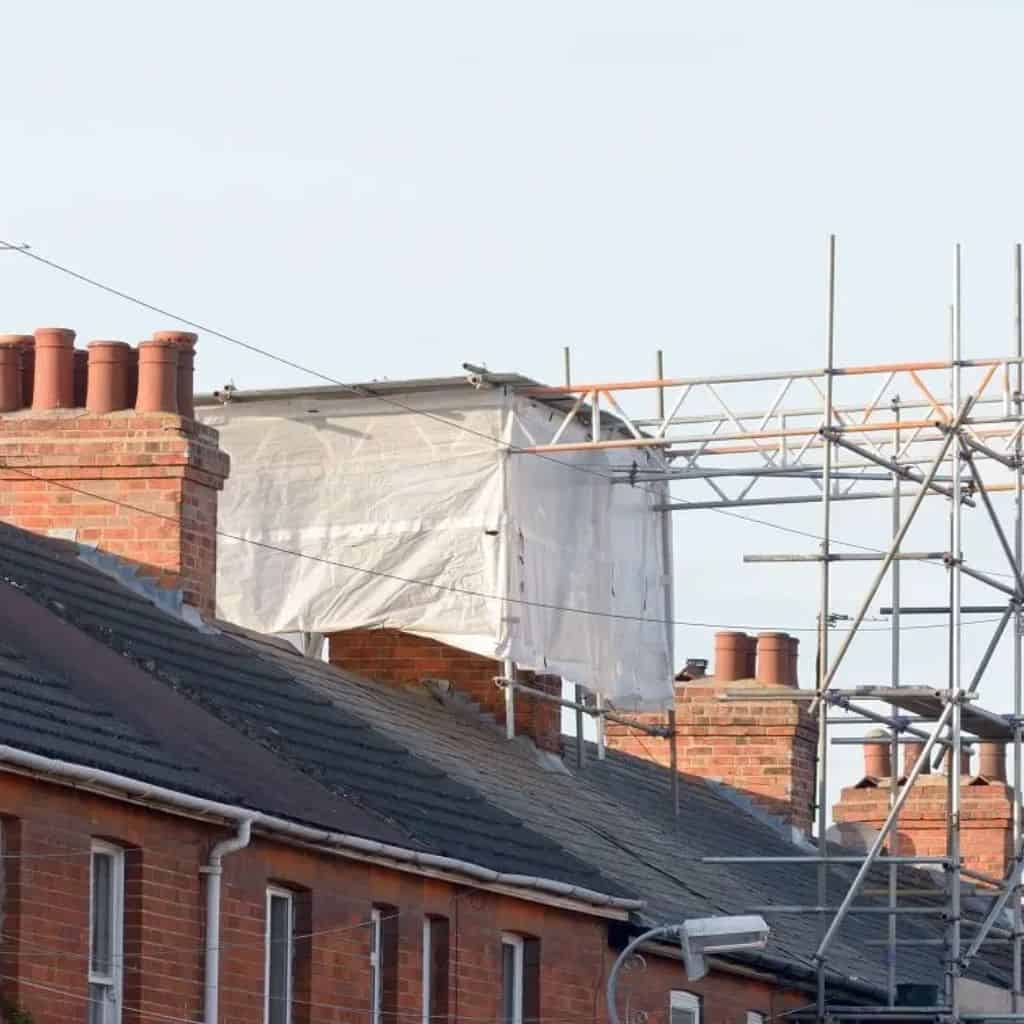 Terraced rooftops with a chimney wrapped in white protective sheeting beside scaffolding, ready for chimney removal.