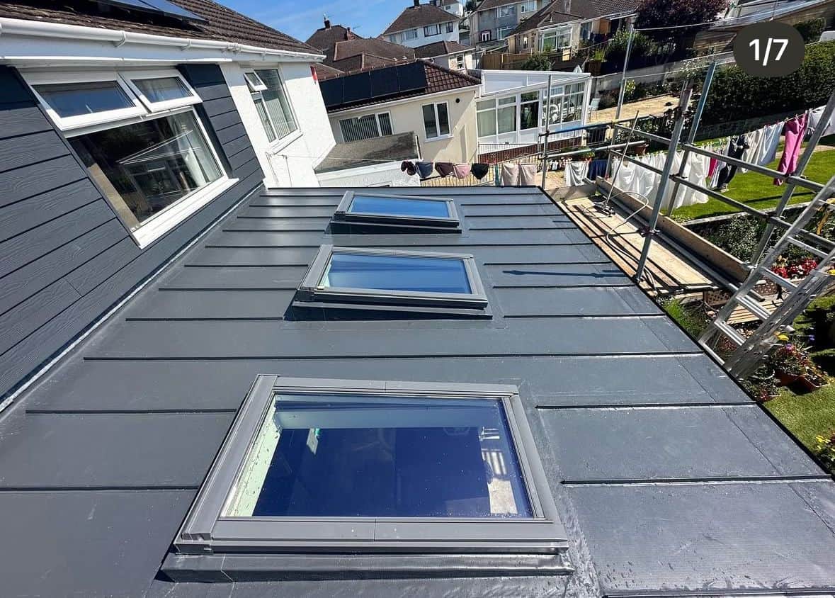 Grey single-ply membrane flat roof with three large roof windows, bordered by grey cladding and scaffolding.