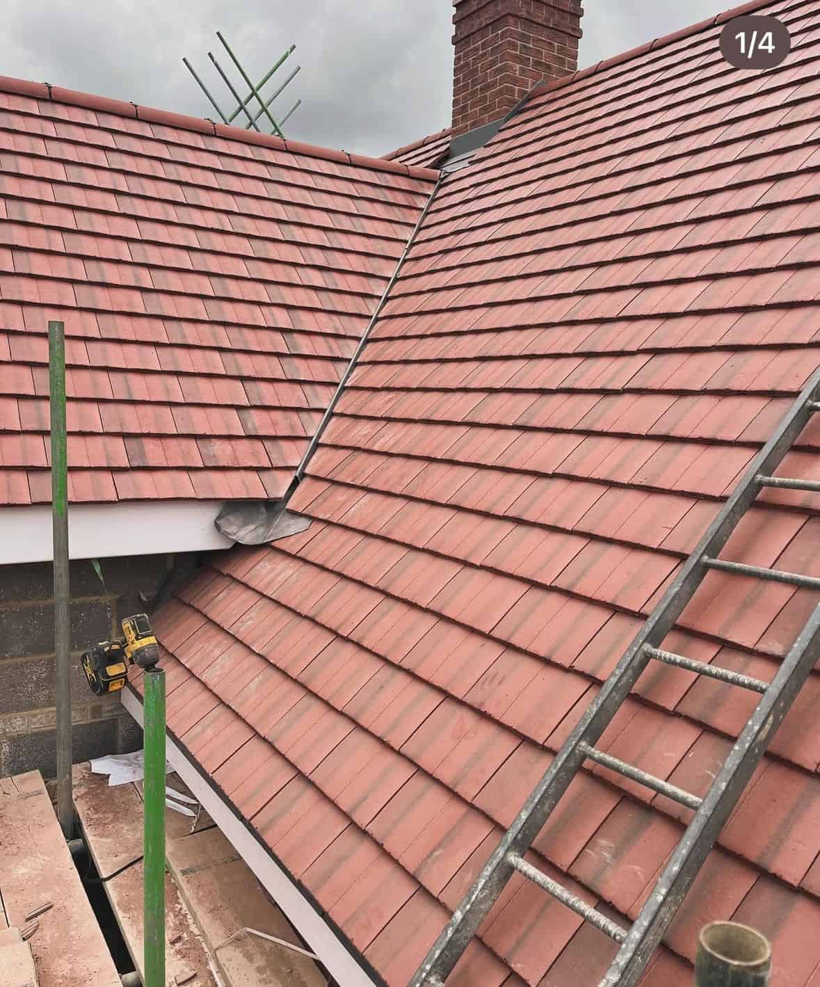 Newly laid red clay tile roof meeting at a lead-lined valley, with a brick chimney and a ladder resting on it.
