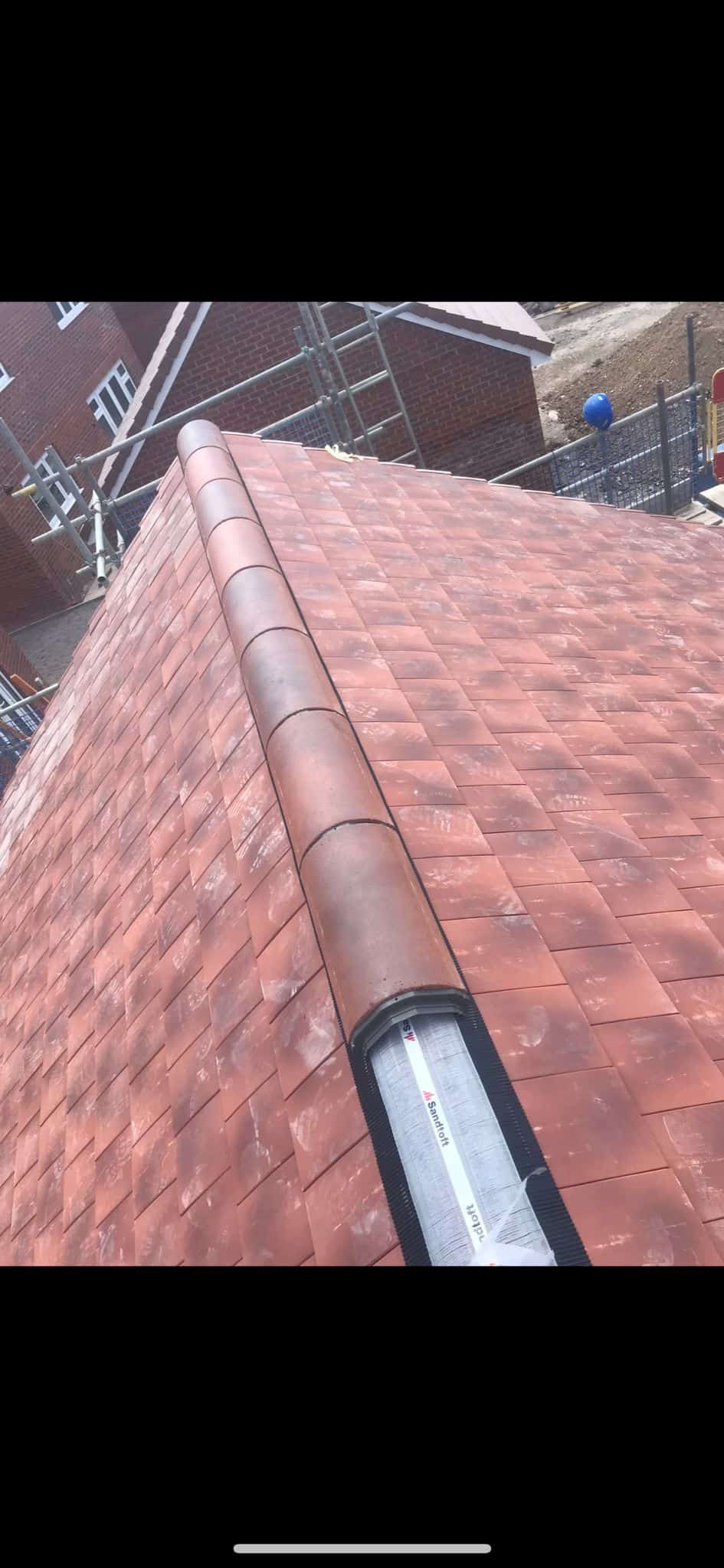 Looking up a steep red clay tiled roof to the ridge, with Sandtoft dry ridge packaging and scaffolding behind.