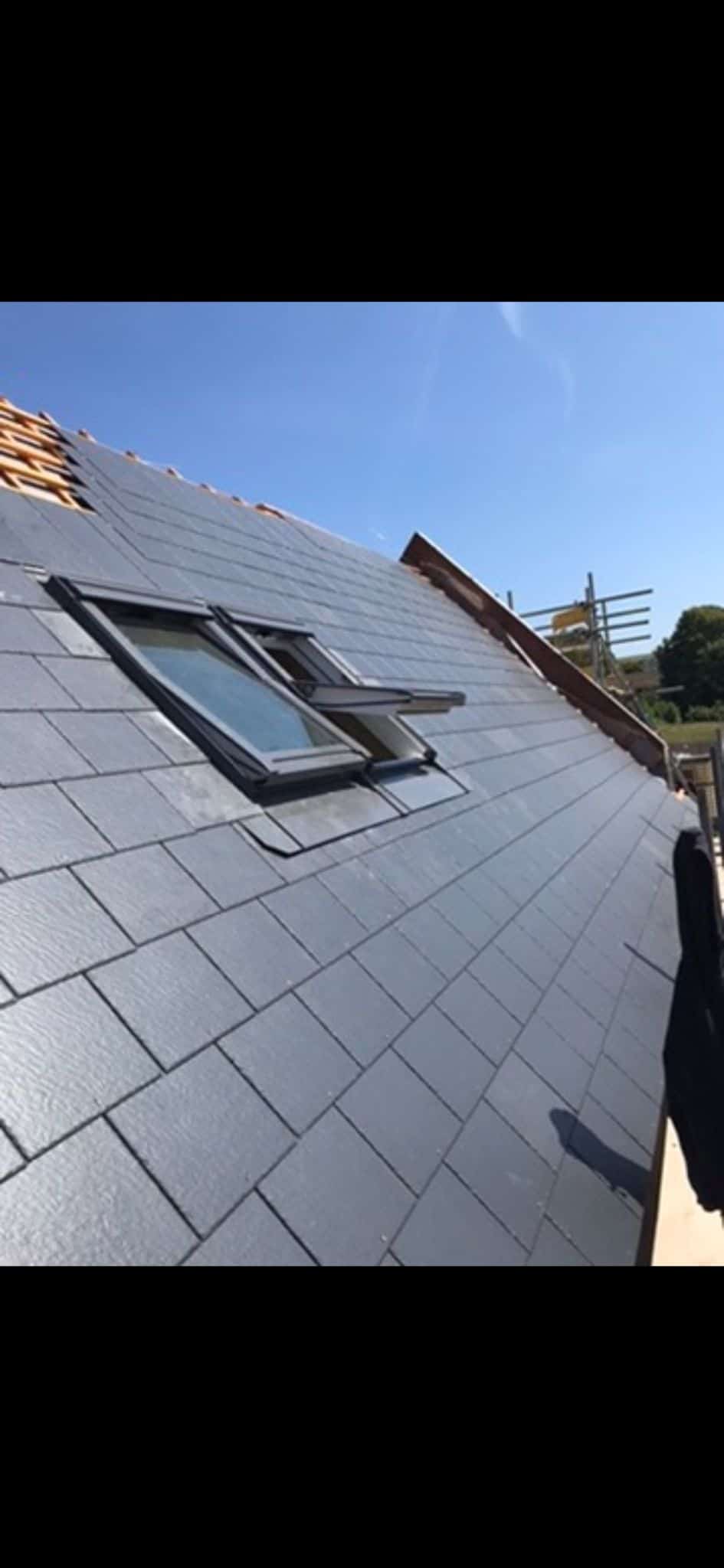 Pitched roof clad in dark grey slate-effect tiles with two Velux roof windows, under a clear blue sky.