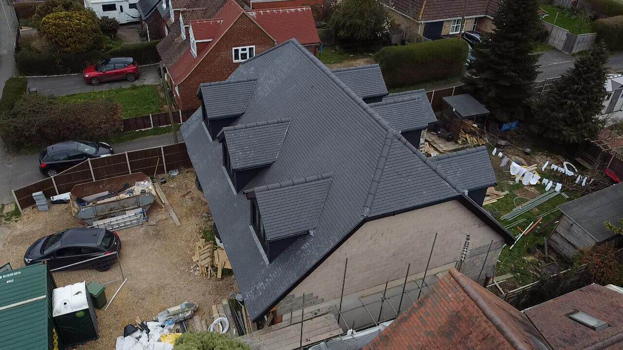 Aerial view of a detached house with a new grey tiled hipped roof and dormers among neighbouring gardens.