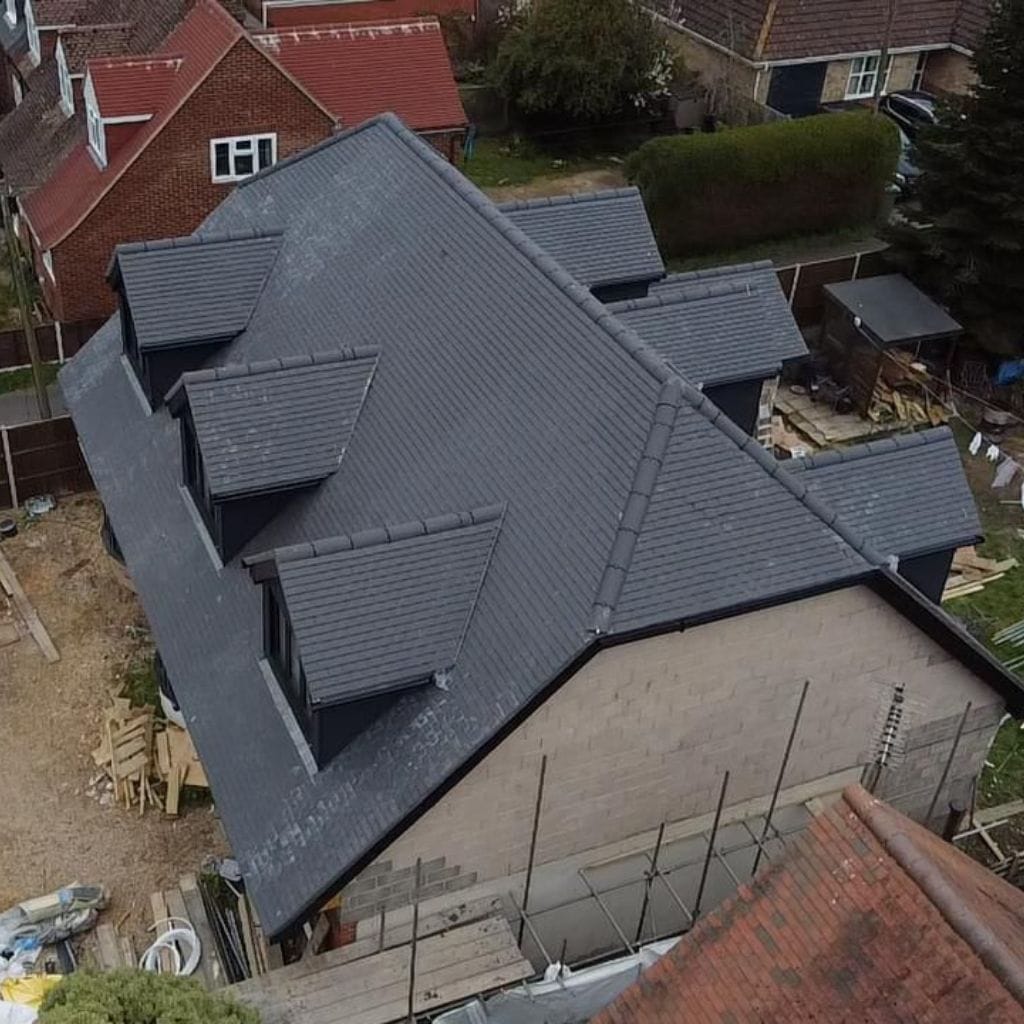 Aerial view of a newly installed grey tiled pitched roof with several gable dormers on a detached house.