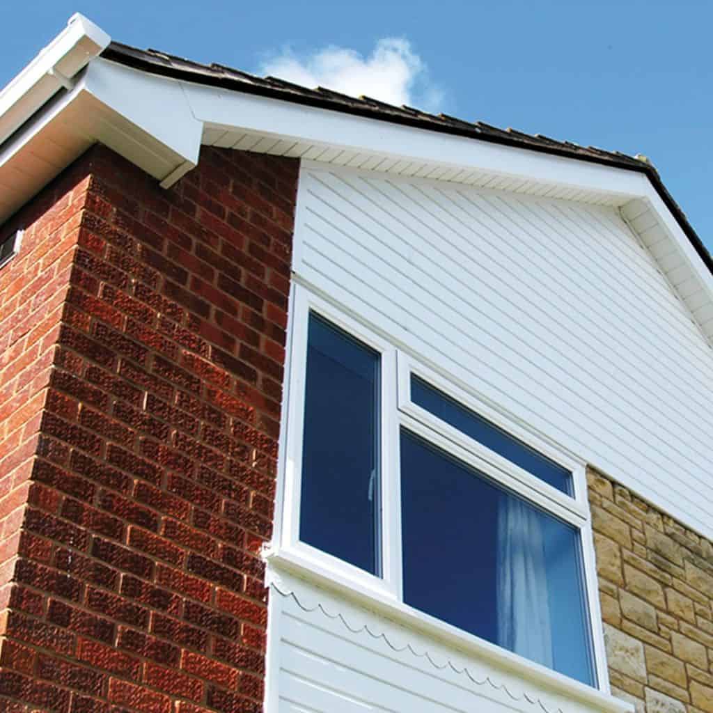 White uPVC weatherboard cladding and soffit on the upper gable of a brick house with a uPVC window against a blue sky.