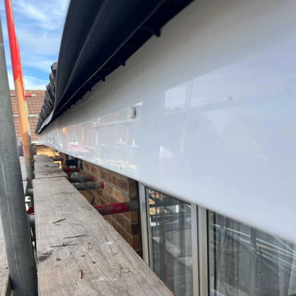 New white uPVC fascia board fitted along a roofline above brick walls, viewed from scaffolding.
