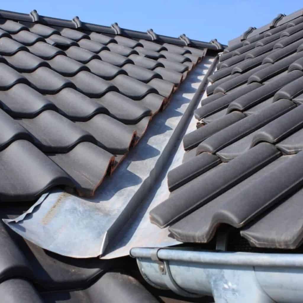 Open lead-lined valley running between two slopes of dark grey interlocking tiles, with a galvanised gutter below.