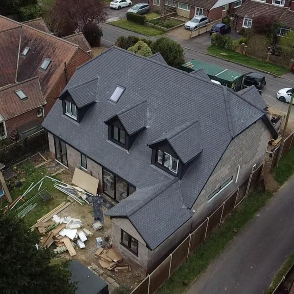 Aerial view of a detached house with a freshly laid grey slate-effect pitched roof and three dormer windows.