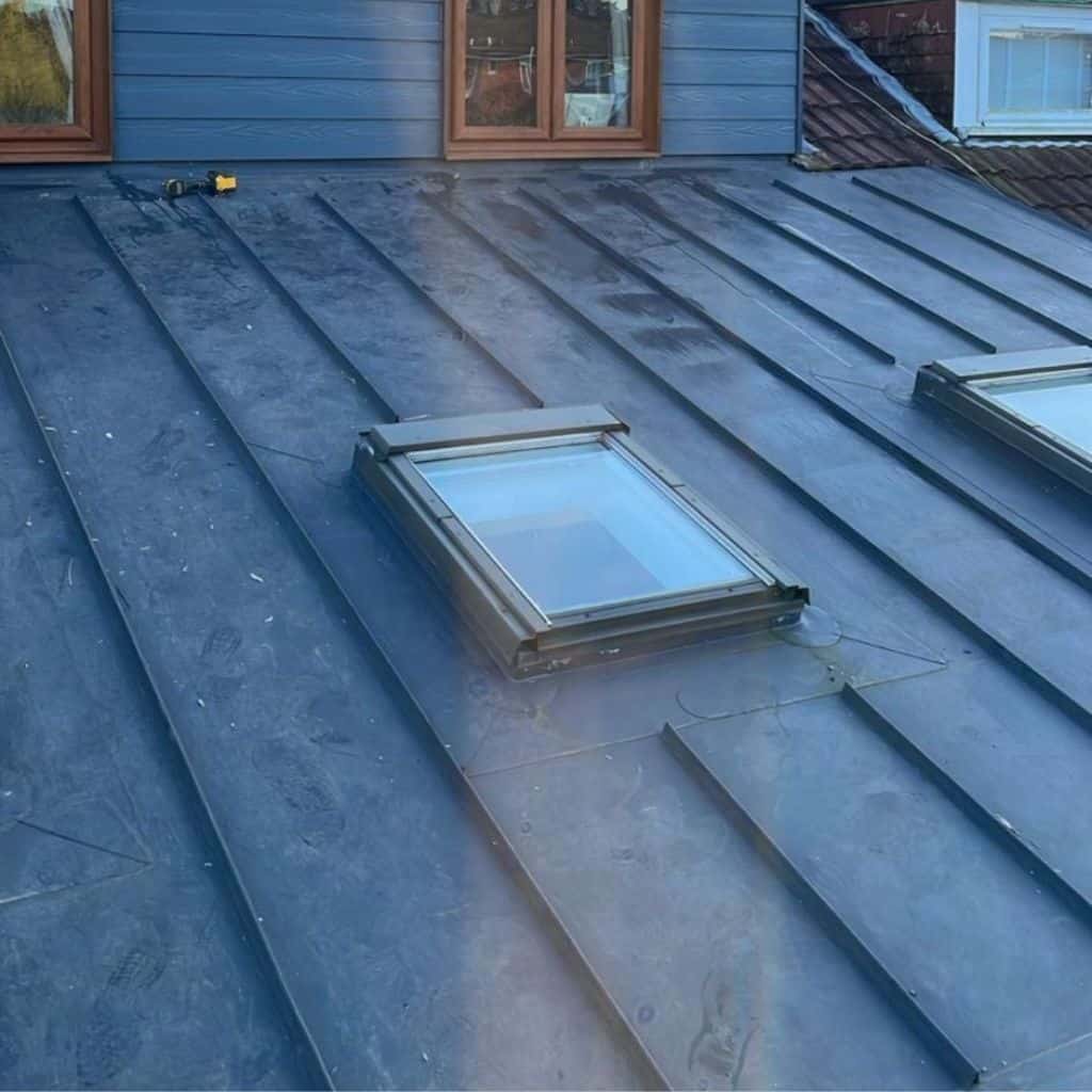 Grey standing-seam single-ply roof on a clad dormer, with two skylight windows set into the membrane.