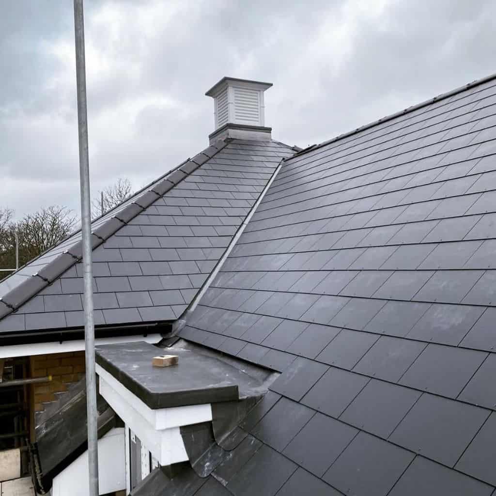 Grey slate roof on a residential property with neat slate courses, a lead valley and a white timber roof vent.