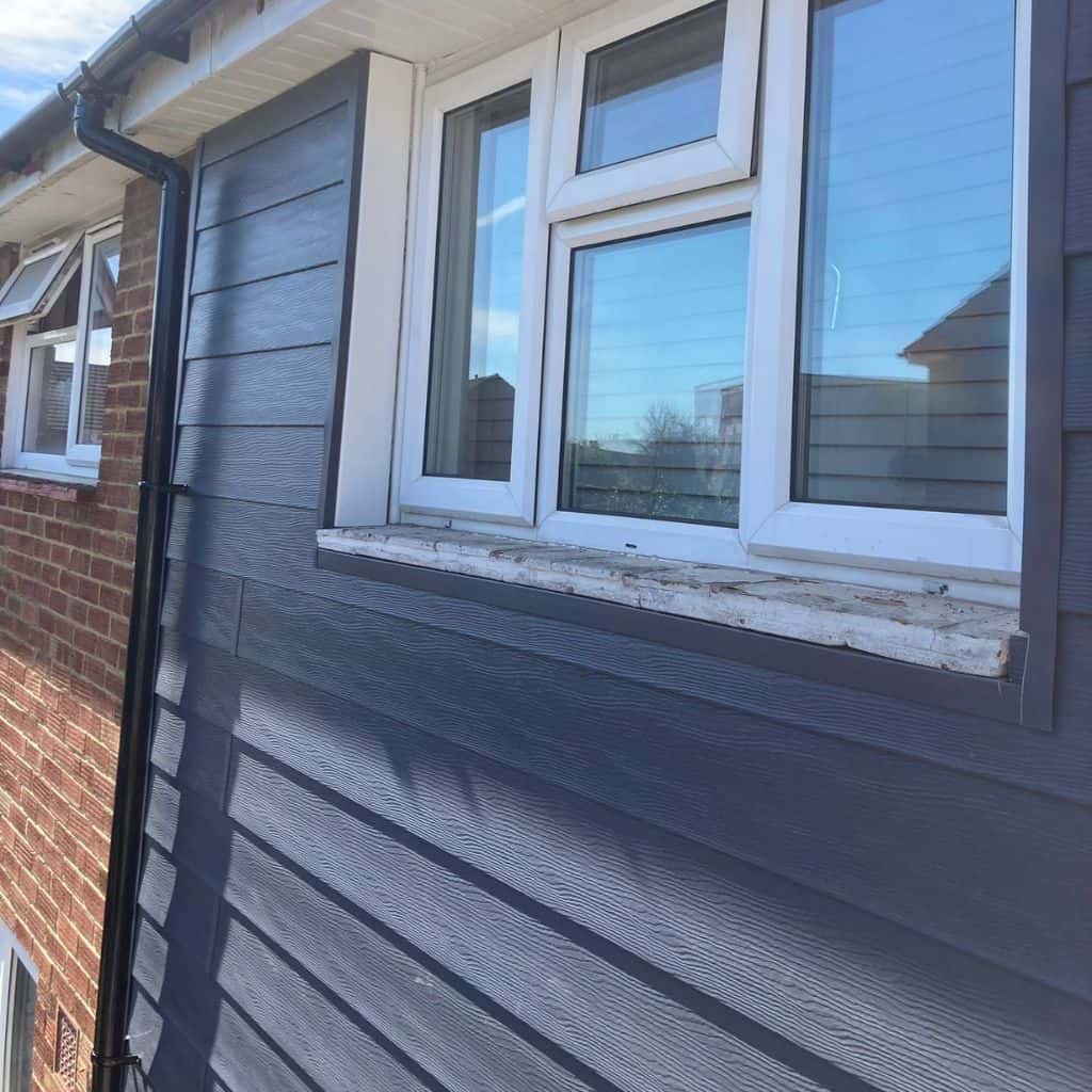 House wall clad in dark grey horizontal weatherboard cladding with a white-framed window and black downpipe.