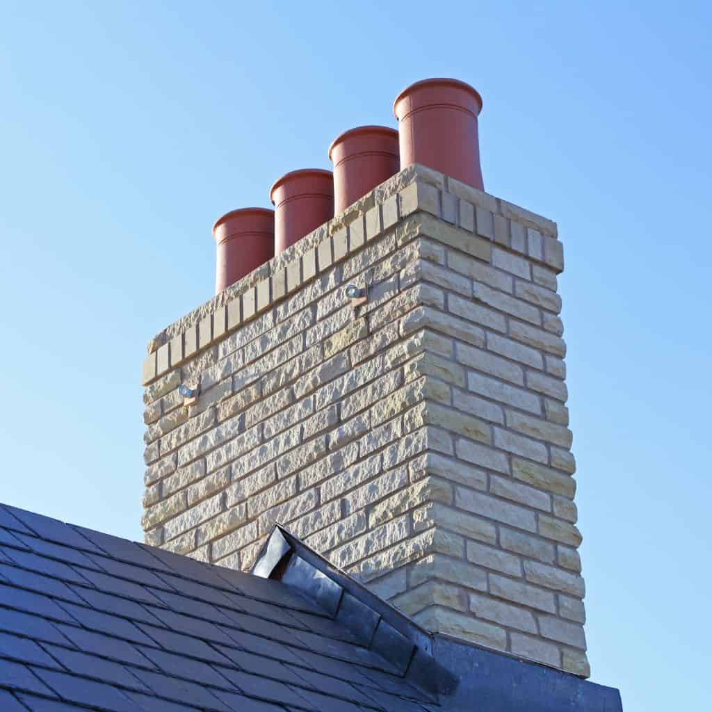 Newly built cream brick chimney stack topped with four terracotta chimney pots against a clear blue sky.