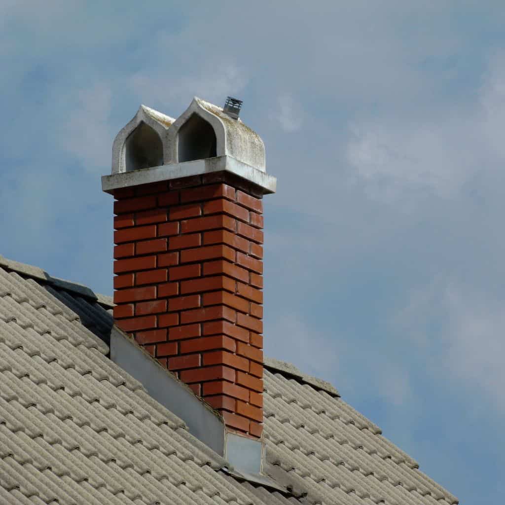 Red brick chimney stack with a twin-pot concrete cap and new chimney cowl, set on a tiled roof against the sky.