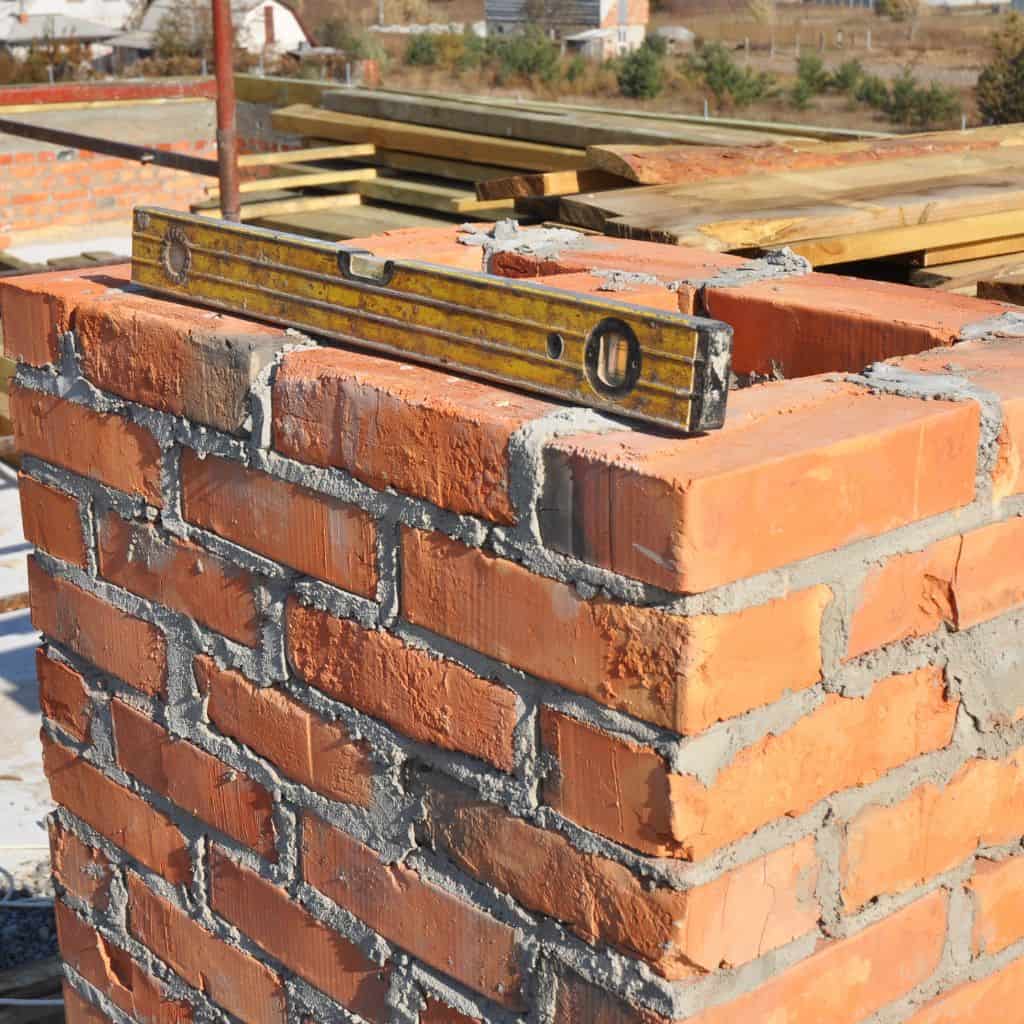 Red brick chimney being rebuilt with fresh mortar, a yellow spirit level resting across the top courses.