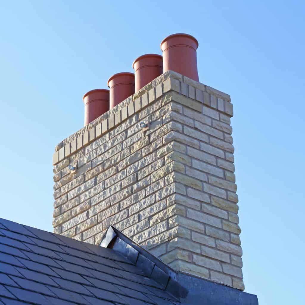 Rebuilt cream brick chimney stack with four red terracotta pots, set on a dark slate roof against blue sky.