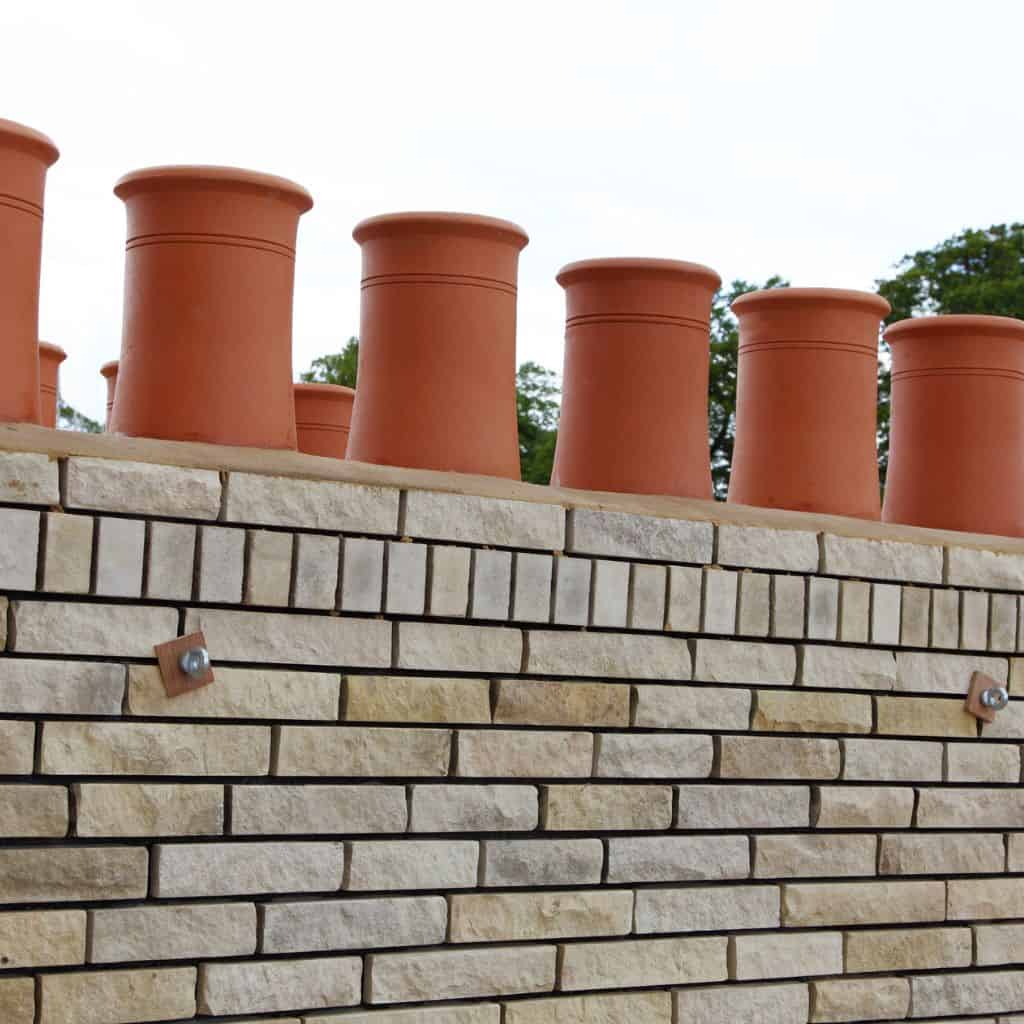 Newly rebuilt cream brick chimney stack topped with several tall terracotta chimney pots against a pale sky.
