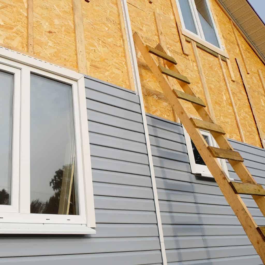 Light grey uPVC weatherboard cladding fitted to a gable end, with a leaded uPVC window and tiled verge against blue sky.