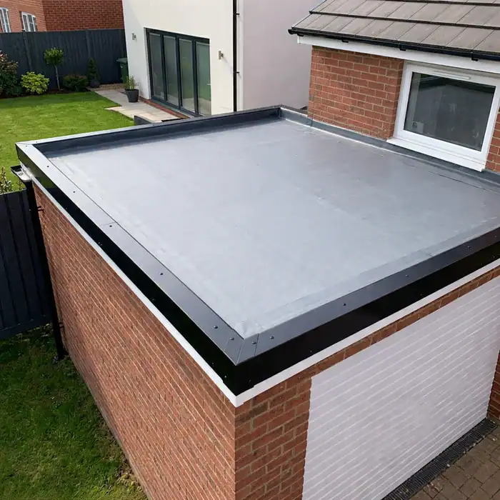 Newly laid grey EPDM flat roof on a garage with neat trims, beside a brick house and lawn.