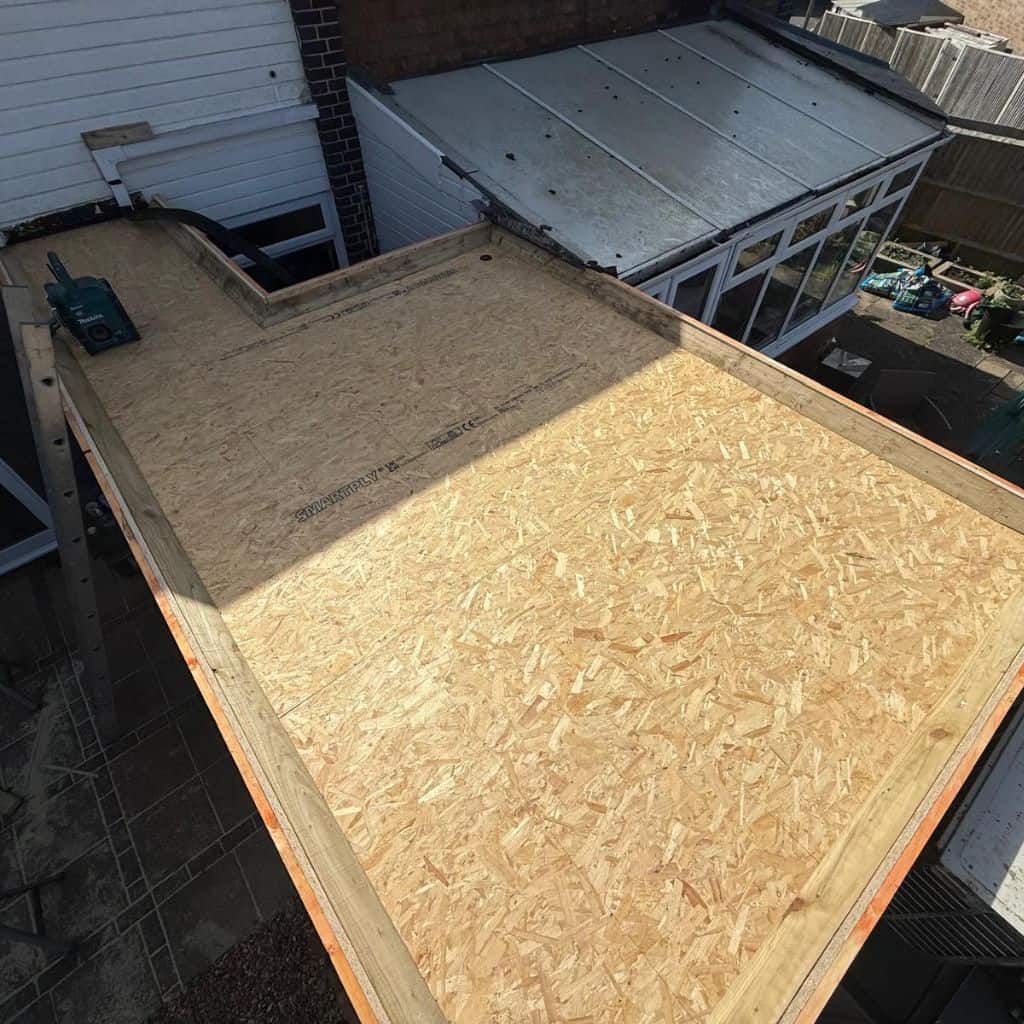 Flat roof deck newly boarded with OSB sheets on timber framing, ready for felt covering, viewed from above.