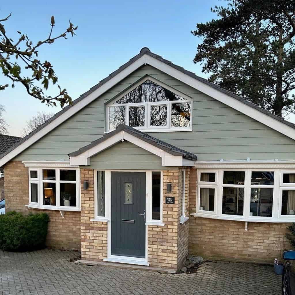House gable clad in sage green fibre cement weatherboarding above a brick porch with a grey composite front door.