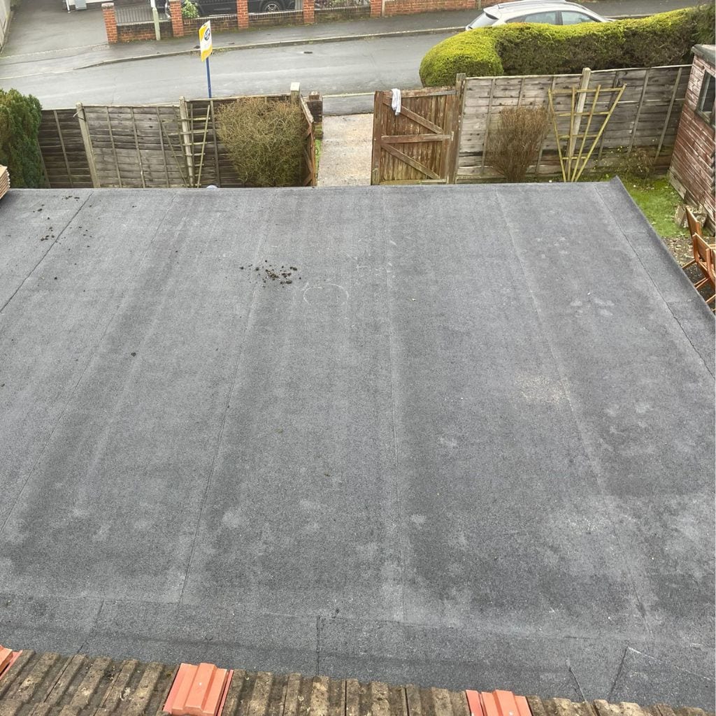 Dark grey GRP fibreglass flat roof fitted with two glazed lantern rooflights, surrounded by tiled pitched roofs.