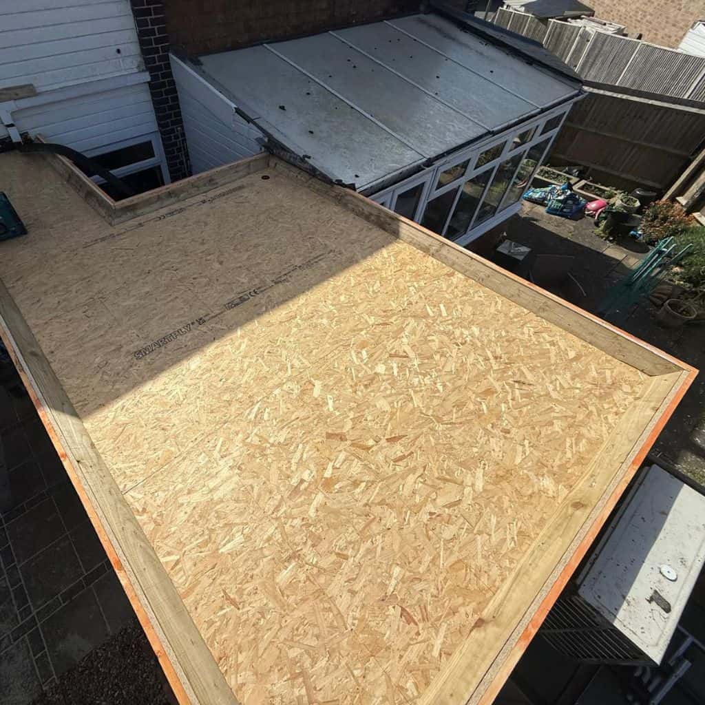 Flat roof of a single-storey extension covered with new dark grey felt, with an old tiled roof alongside.
