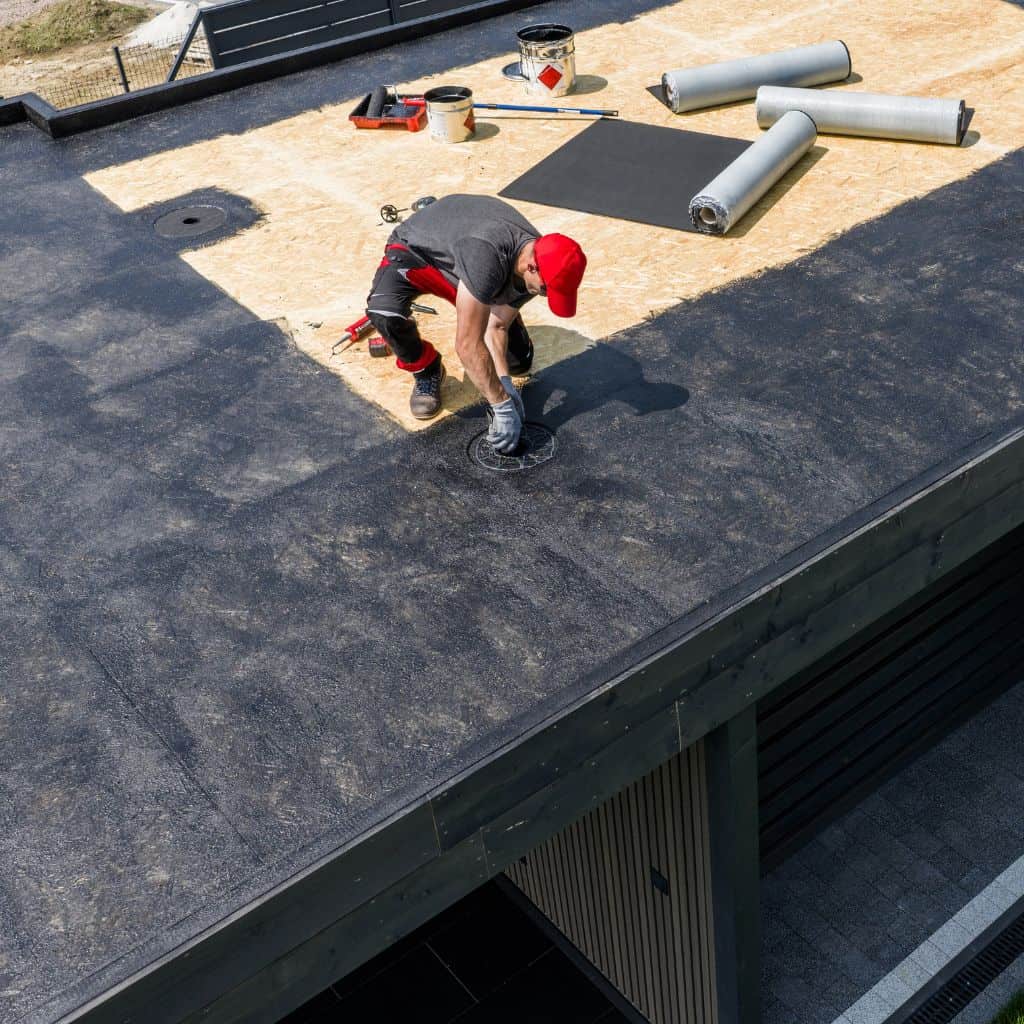 Newly laid felt flat roof with a red gas bottle, hose and tools, set between brick rear walls of a house.
