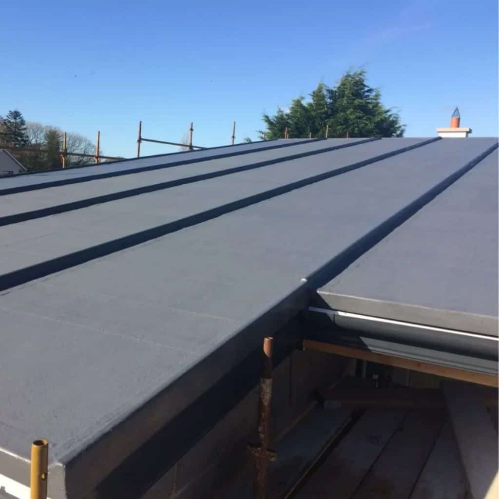 Smooth grey GRP fibreglass flat roof with raised seam trims, under a clear blue sky with a chimney beyond.