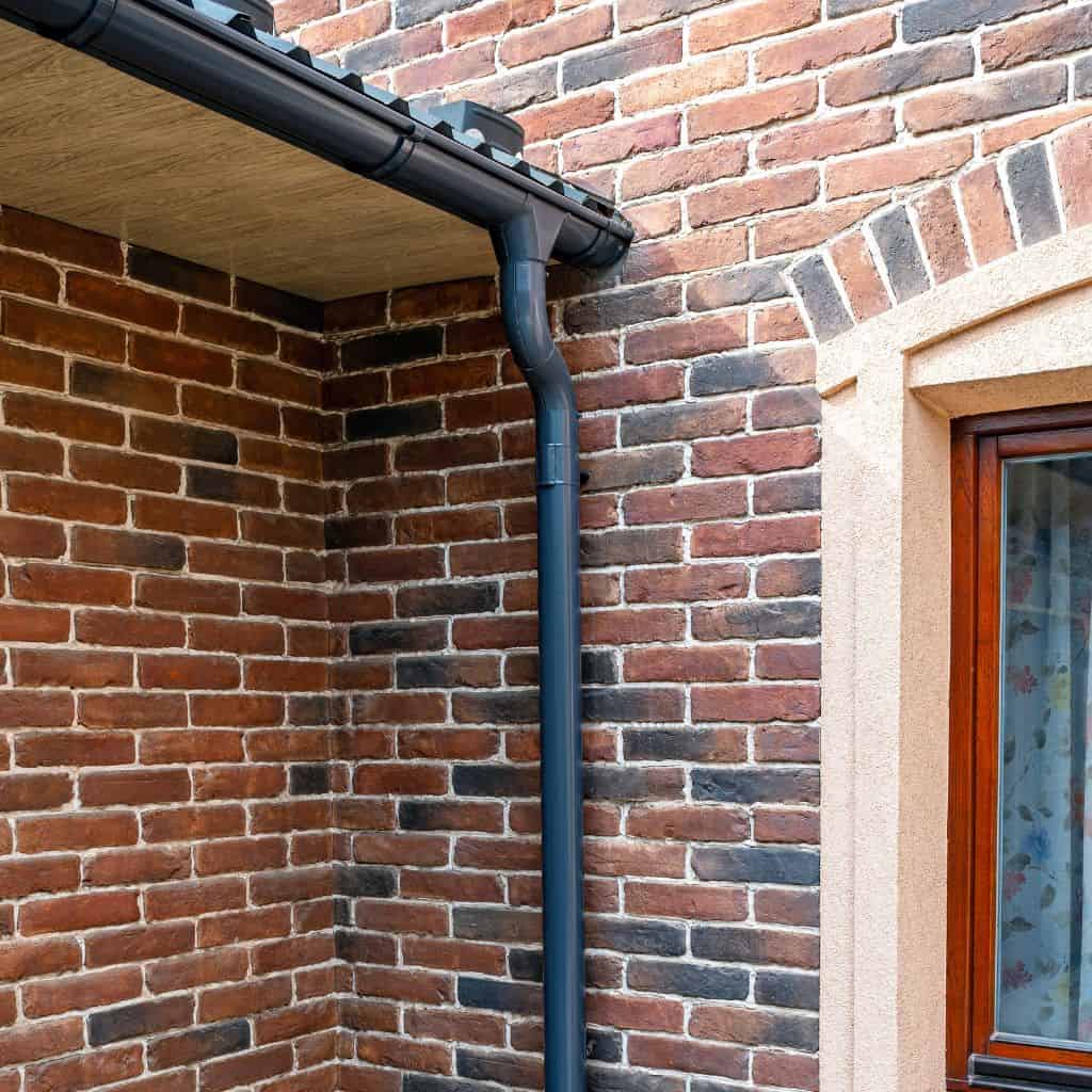 Anthracite grey gutter and downpipe fitted to fascia on a multi-toned red brick house corner.