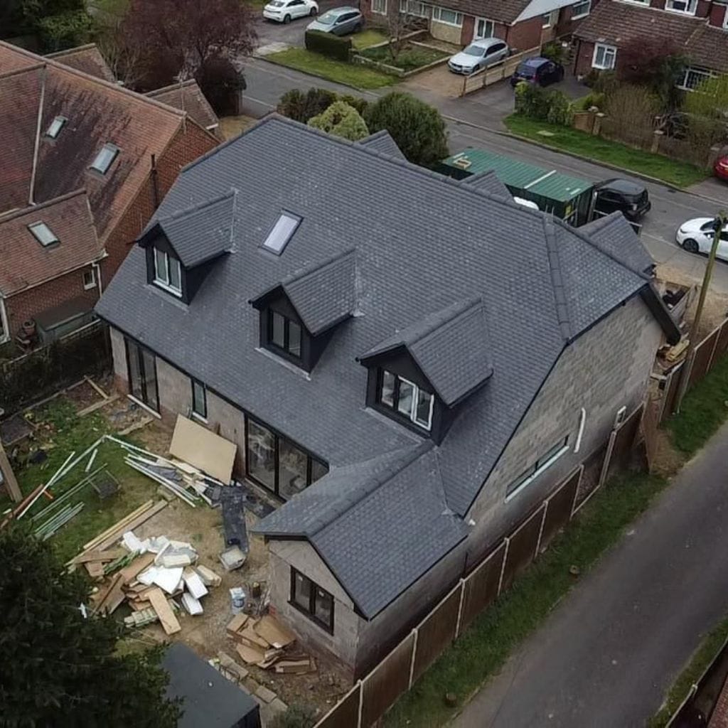 Aerial view of a large house with a newly laid grey slate-tiled roof and three dormer windows, with materials on site.