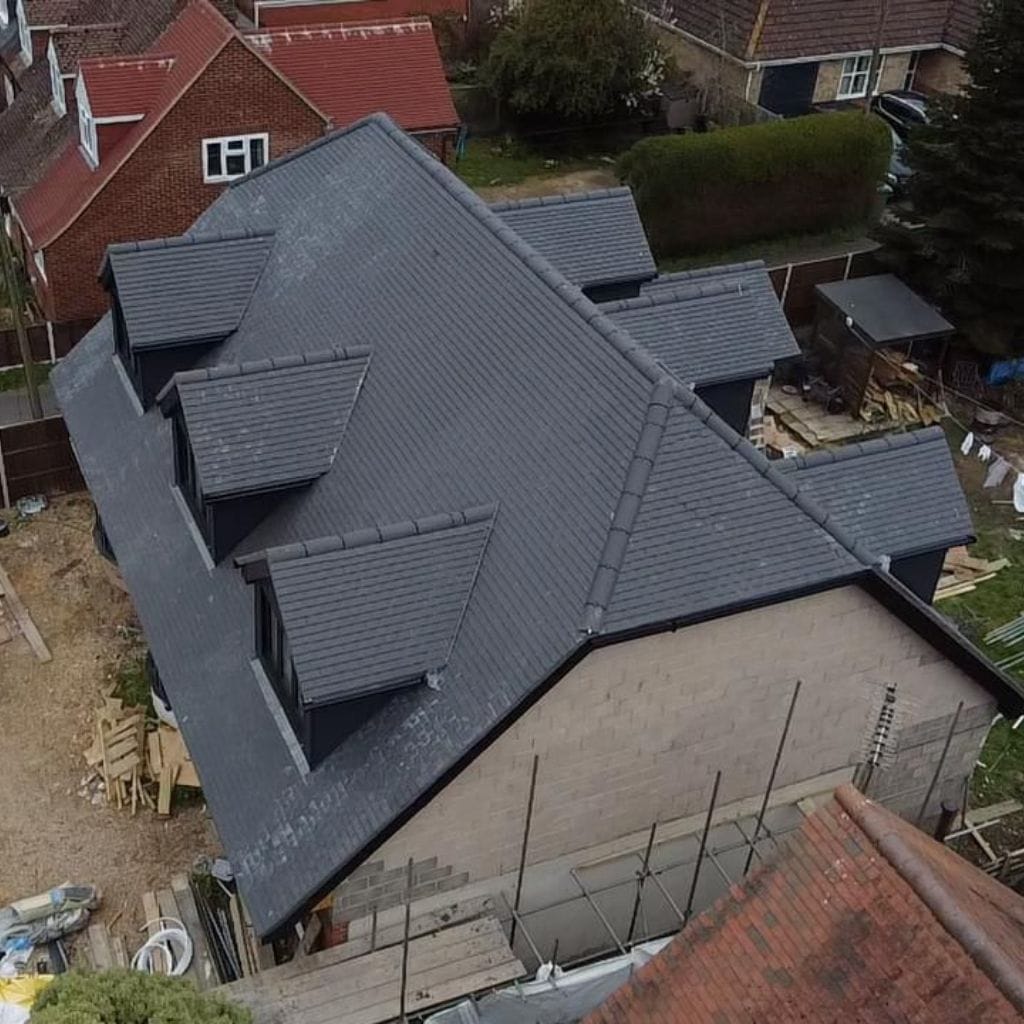 Aerial view of a detached house with a new dark grey tiled roof and four dormer windows, scaffolding to the rear.