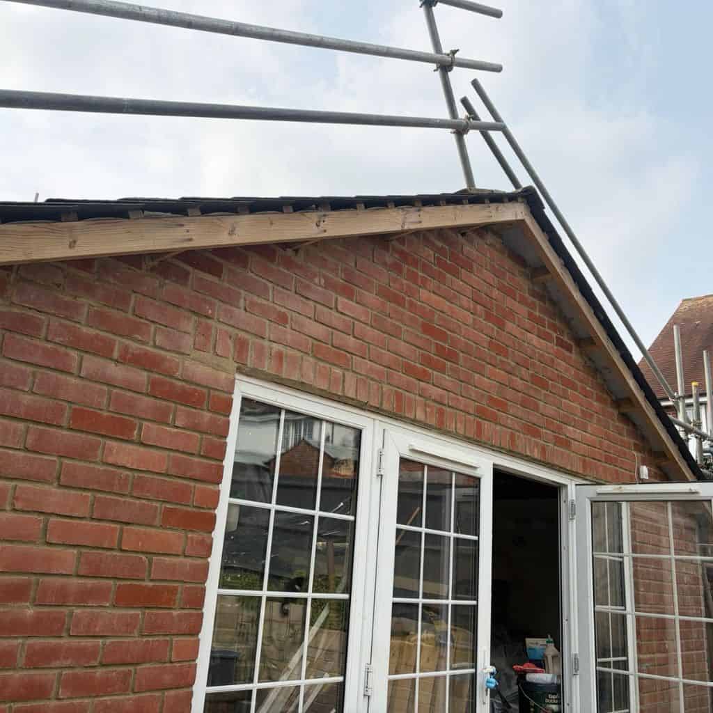 Brick gable end with the old fascia and felt stripped back at the roof edge, scaffolding poles above.