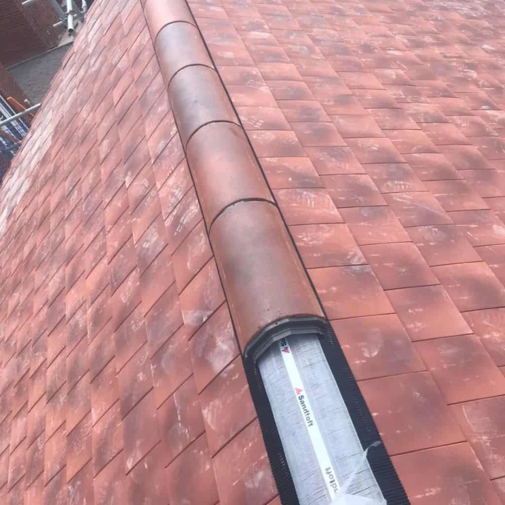 Red clay tile roof with a terracotta half-round ridge being bedded, showing Sandtoft dry-ridge roll along the apex.