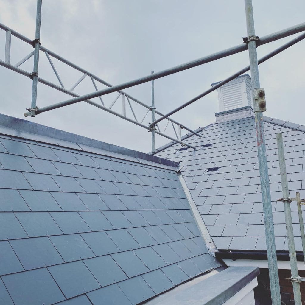 Dark grey slate roof meeting at a lead-lined valley, framed by scaffolding poles under a pale sky.