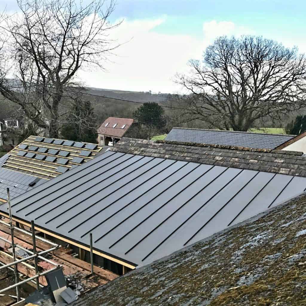 Section of dark grey single-ply membrane roofing on a building, with a TV aerial and cloudy sky above.